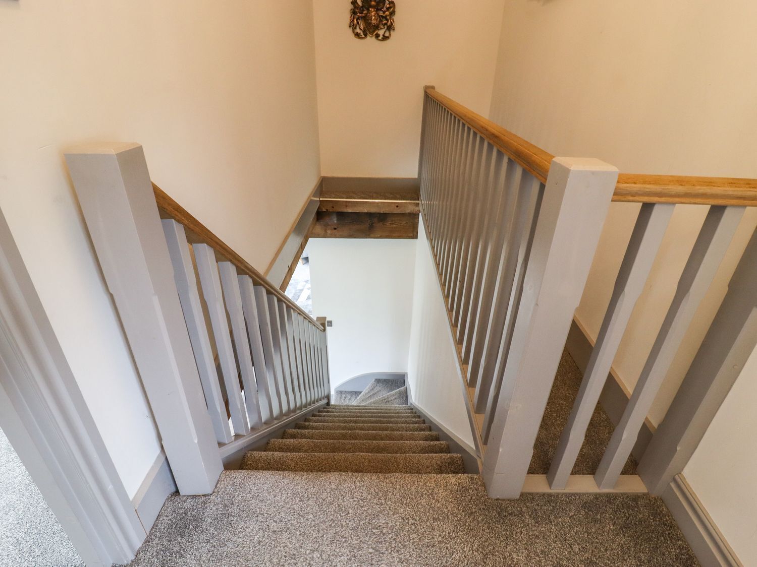 Un escalier avec des rampes en bois et des marches recouvertes de moquette, menant à l’étage supérieur.