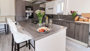 A modern kitchen with a central island, bar stools, and a dining area. - Cunliffe Barn (Shipley)