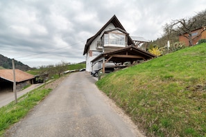 A rural road leading to a house with a sloped roof and a balcony.