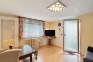 A living room with a wooden floor, a dining table, chairs, a TV, a radiator, and a door with a frosted glass panel.