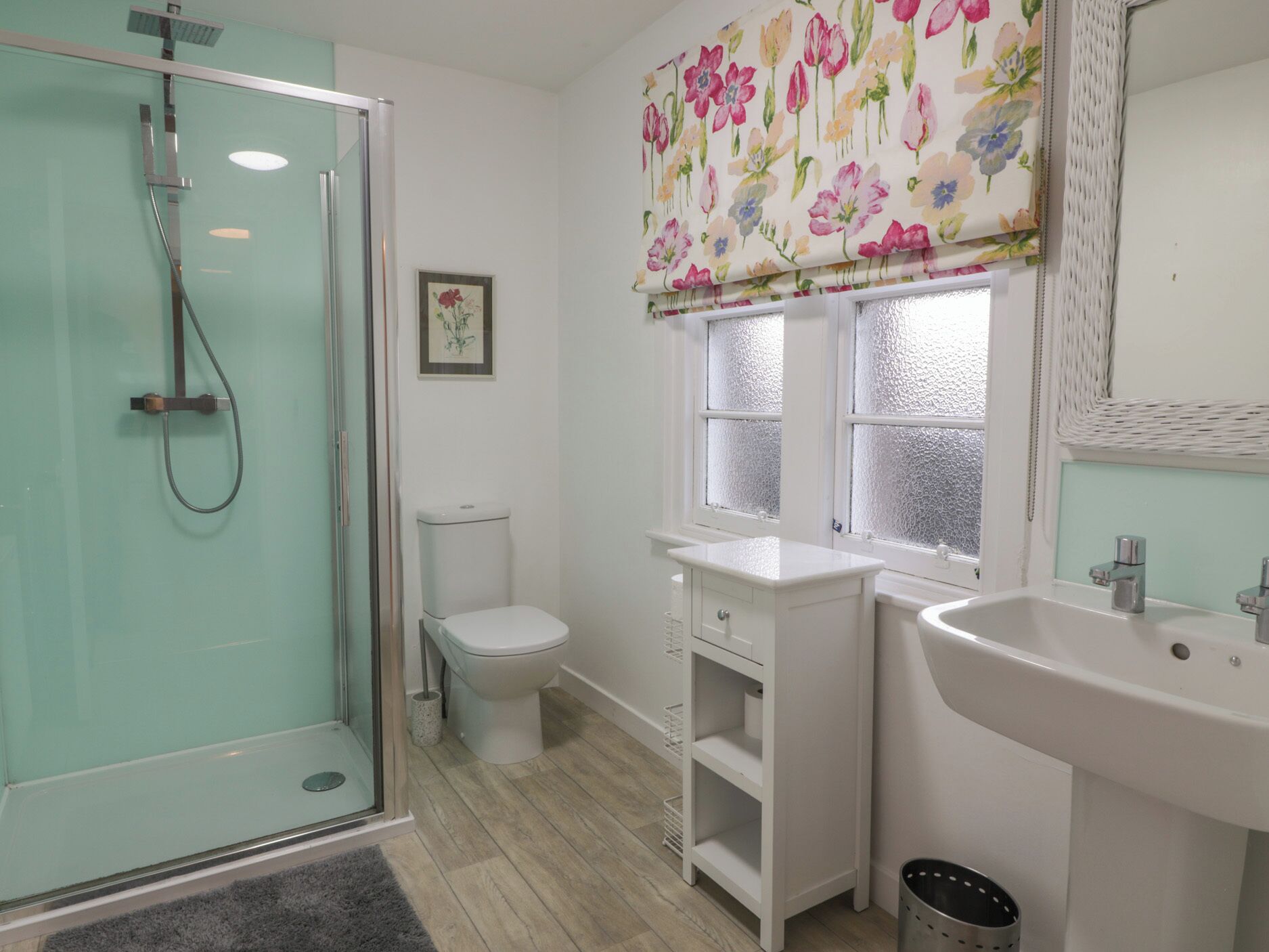 A bathroom with a glass shower enclosure, a toilet, a sink, and a window with frosted glass.