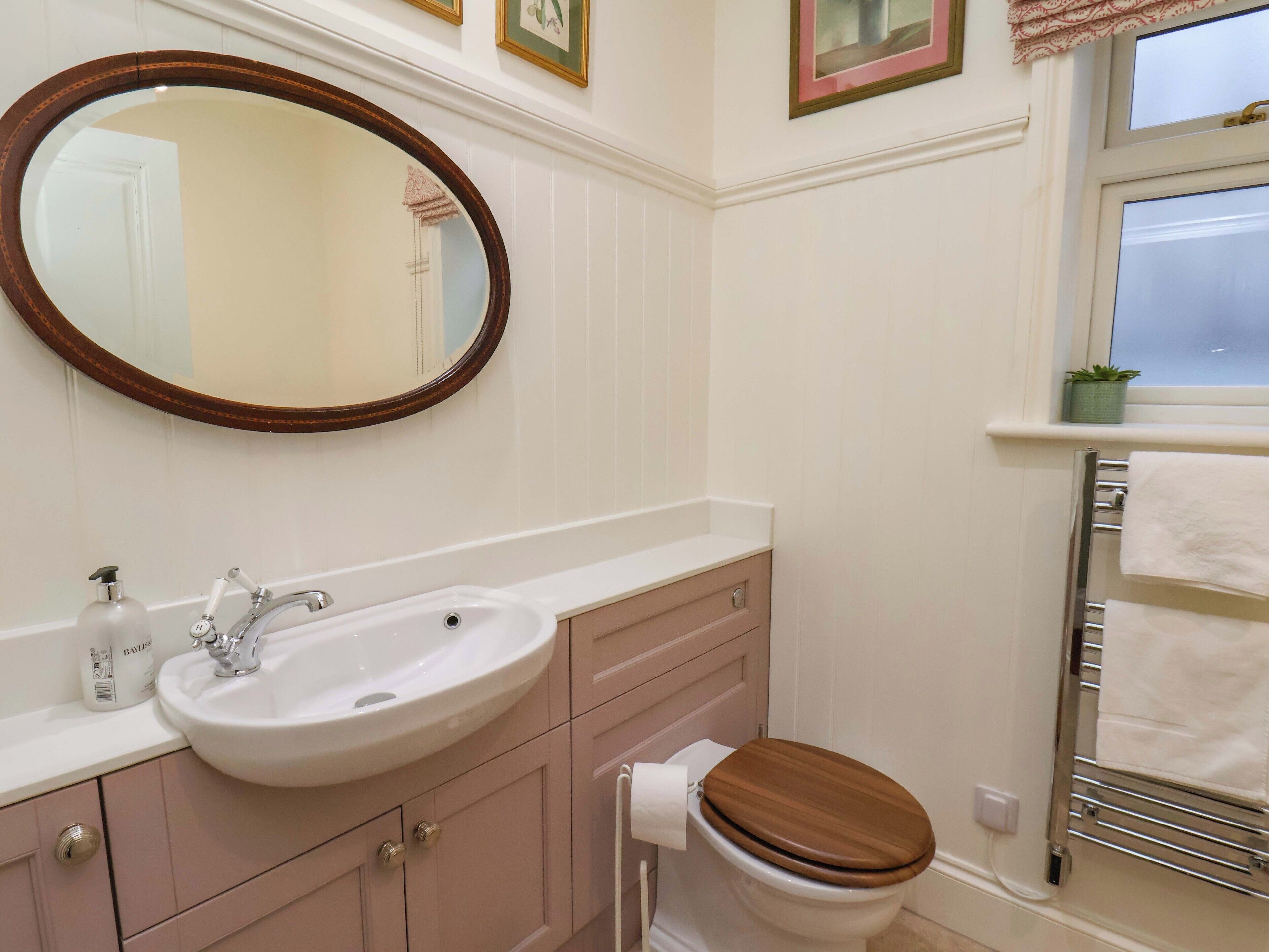 A bathroom with a white sink, wooden vanity, a mirror, a toilet, and a towel rack.