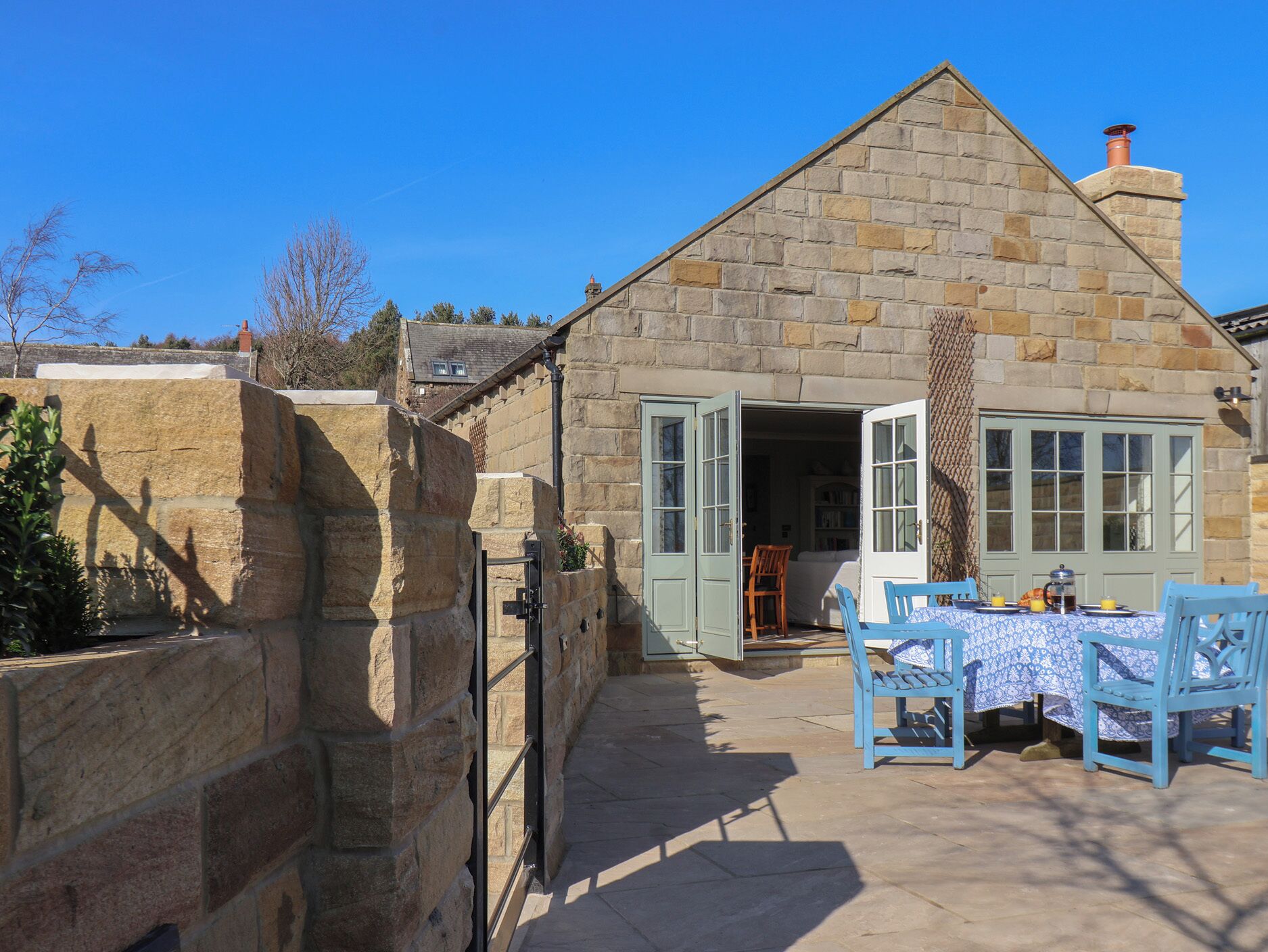 A stone cottage with a large open door, a small table with chairs, and a clear blue sky.