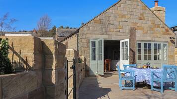 A stone cottage with a large open door, a small table with chairs, and a clear blue sky.