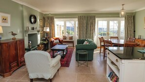 A cozy living room with a green sofa, a checkered armchair, and a dining area with a wooden table and chairs. - Roding Cottage (Whitby)