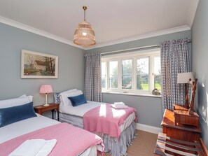 Une chambre avec deux lits, une fenêtre avec des rideaux, un tableau au mur et une lampe sur une table de chevet.