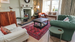 A cozy living room with a fireplace, green sofa, checkered armchair, and a patterned rug. - Roding Cottage (Whitby)