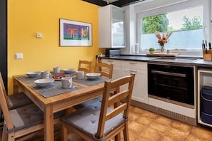 A kitchen with a dining table, chairs, a stove, and a window with a view of greenery.