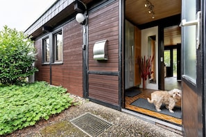 A modern house with a wooden exterior, a dog standing at the entrance, and a doorbell.