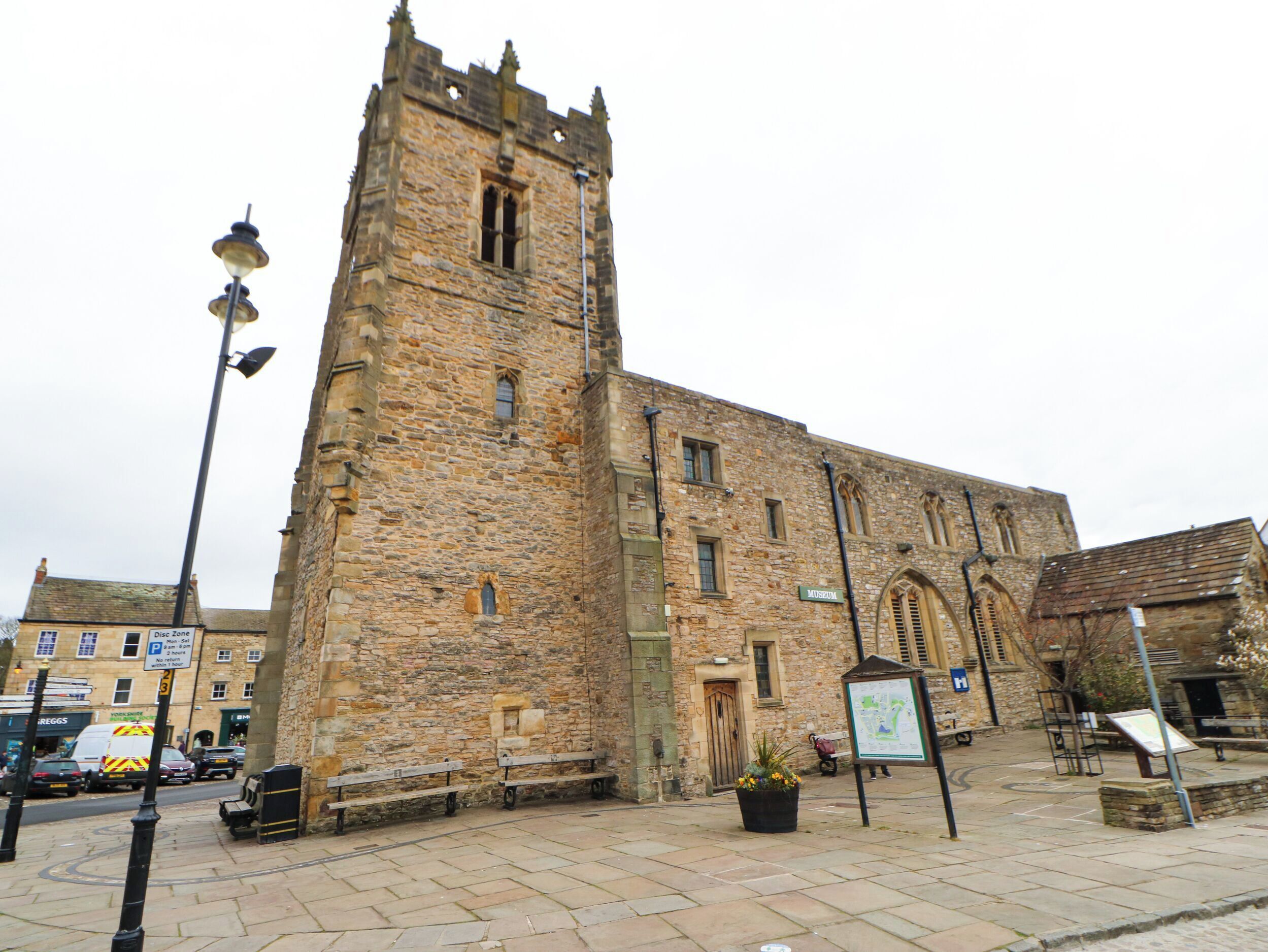 A historic stone building with a tall tower, a paved courtyard, and a signboard.