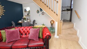 A living room with a red leather sofa, a staircase, and a kitchen in the background.