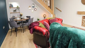 A modern living room with a red leather sofa, a dining table with chairs, and a staircase.