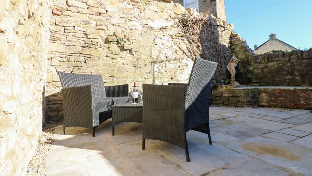 An outdoor patio with stone flooring, wicker furniture, and a stone wall.