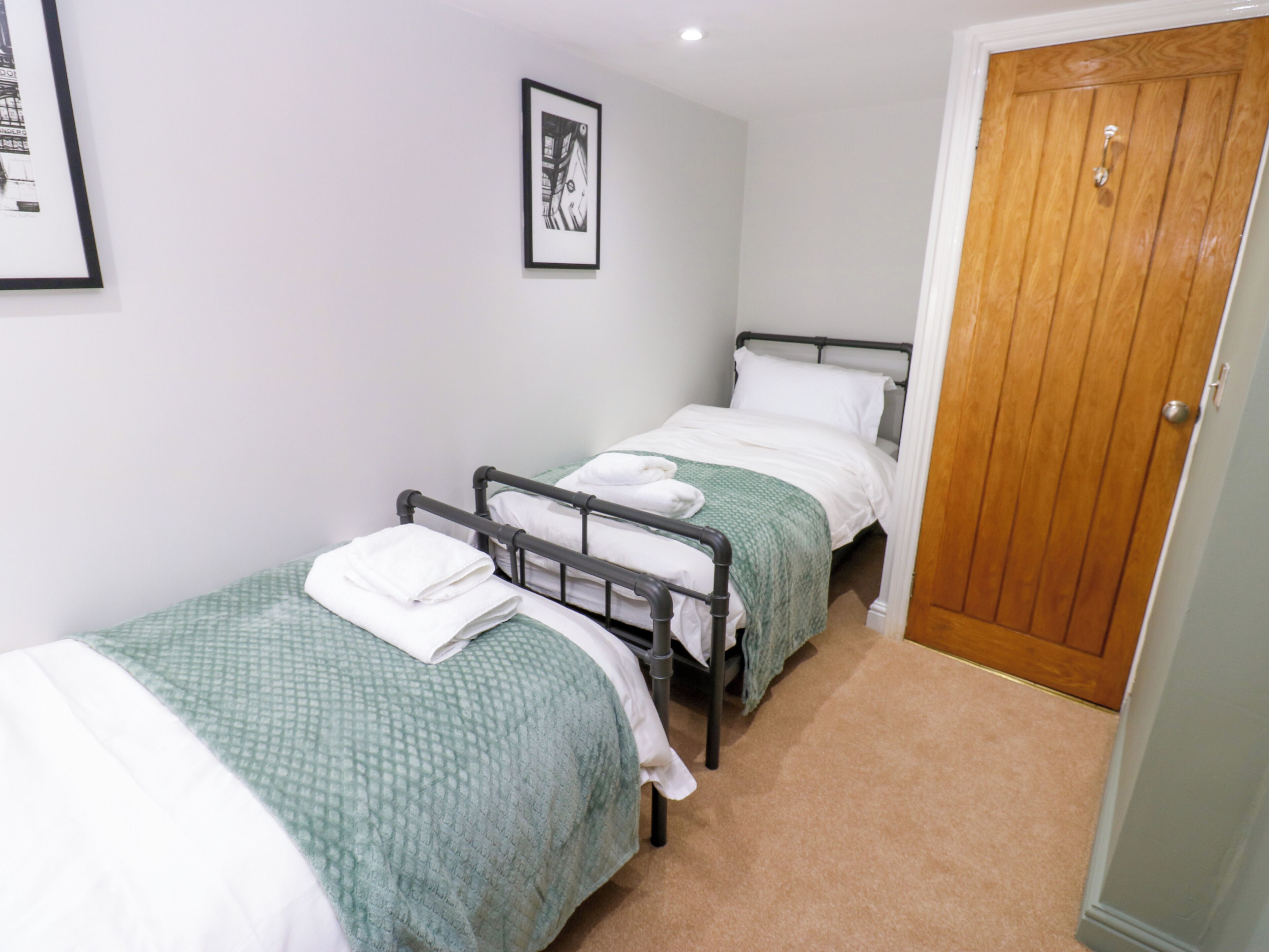 A small, clean room with two single beds, a wooden door, and a framed picture on the wall.