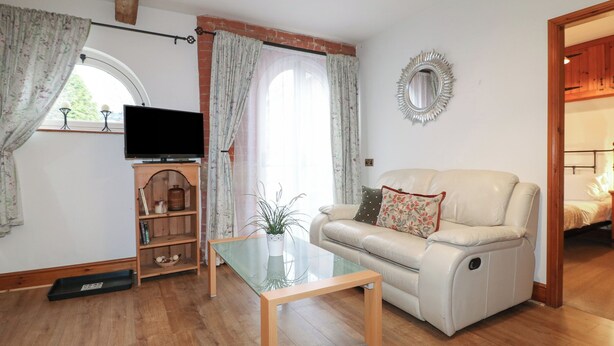 A living room with a sofa, a glass coffee table, a television, and a wooden cabinet. - Stables (Derby)