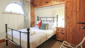 A bedroom with a metal bed frame, a wooden wardrobe, a small bedside table, and a window with curtains. - Stables (Derby)