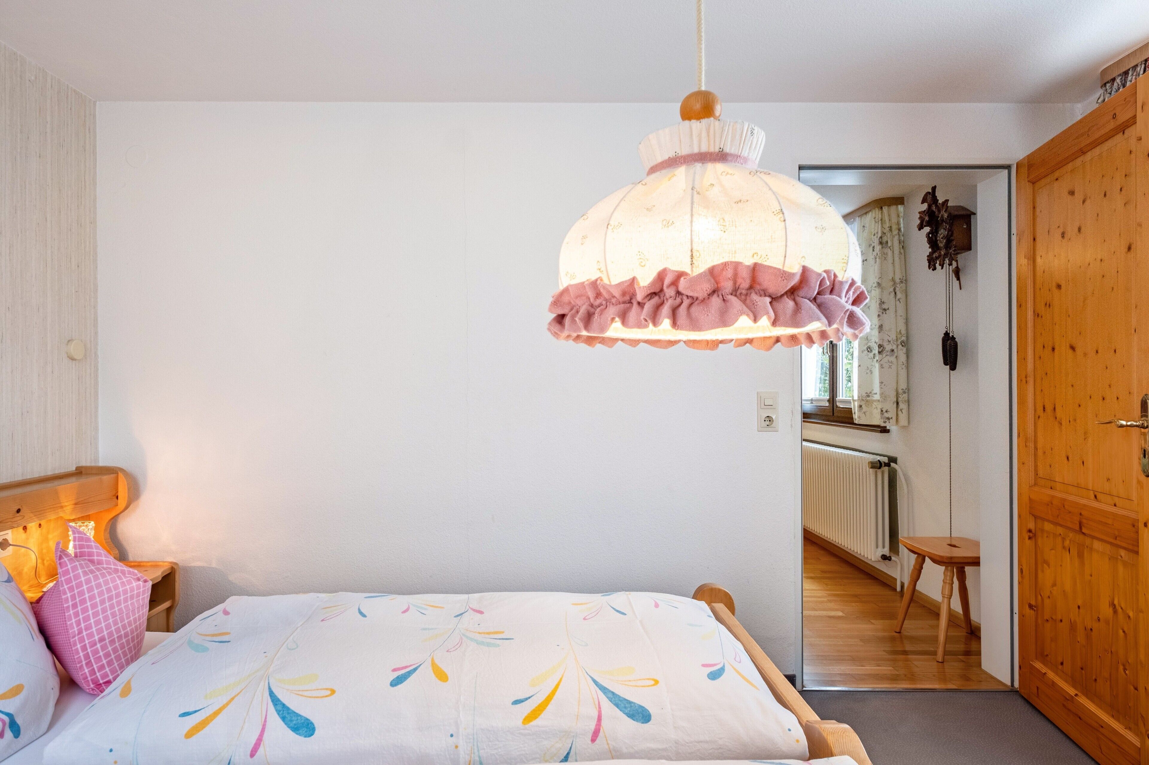Ein Schlafzimmer mit Bett, einer Hängelampe, einer Holztür und Blick in einen anderen Raum.