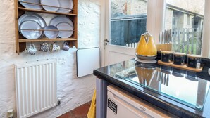 A kitchen with a wooden dish rack, a yellow kettle, and jars labeled 'tea,' 'coffee,' and 'sugar' on the counter. - Briar Orchard Annex (Chard)