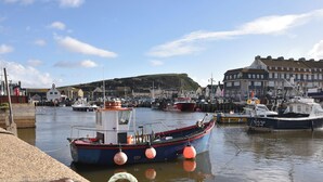A harbor with boats docked, a building with a sign reading "St. John's Church", and a hill in the background. - Briar Orchard Annex (Chard)
