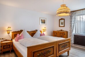 A double bed with a wooden headboard, two bedside tables with lamps, a radiator, and a window with curtains. - Apartment 'Rathäusle I' with Shared Terrace, Shared Garden and Wi-Fi (Titisee-Neustadt)