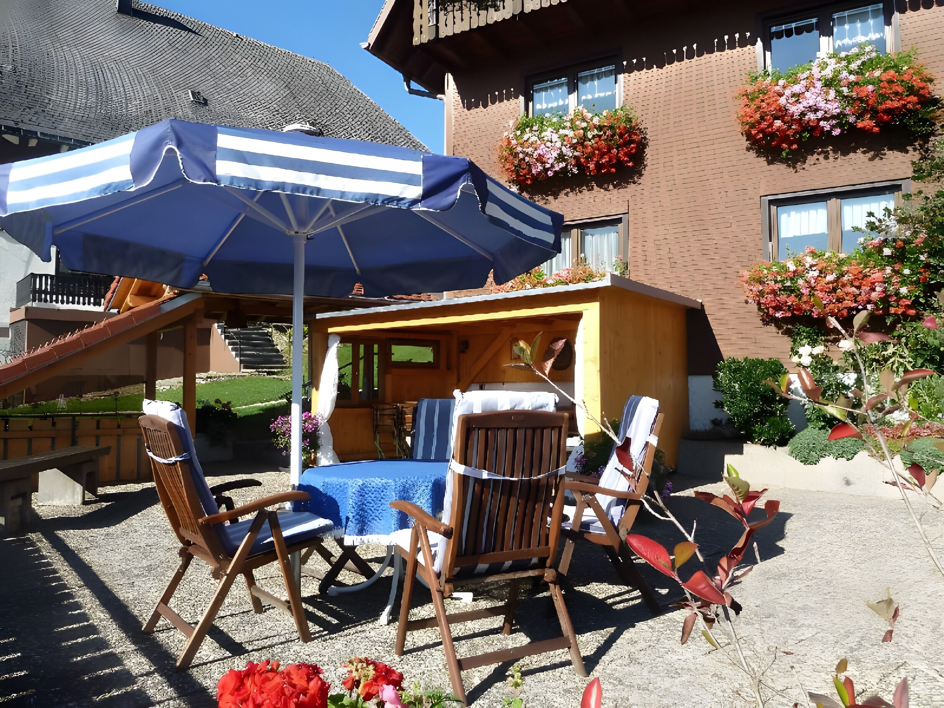 Une terrasse avec une table et des chaises, un parasol bleu et un bâtiment en briques agrémenté de jardinières.