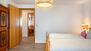 Een slaapkamer met een bed, een houten garderobe, een kroonluchter en een nachtkastje met een lamp.