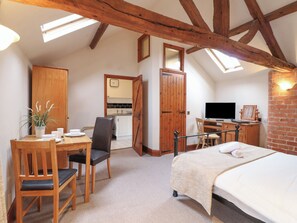 A cozy attic bedroom with a wooden ceiling, a bed, a desk with a computer, and a dining area with chairs and a table.
