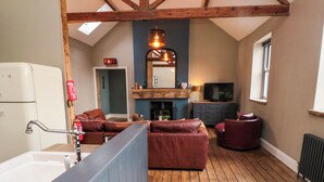 A cozy living room with a fireplace, leather sofas, a television, and a wooden floor. - Cedar Cottage (Barnard Castle)