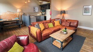 A cozy living room with a leather sofa, a wooden coffee table, and a dining area with a bench. A kitchen is visible in the background. - Cedar Cottage (Barnard Castle)