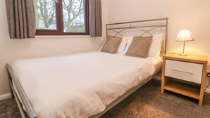 A single bed with a metal frame, a bedside table with a lamp, and a window with curtains.