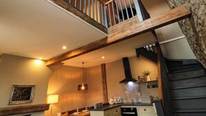 A multi-level interior with exposed wooden beams, a staircase, and a kitchen area with modern appliances. - Ash Cottage (Barnard Castle)