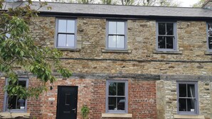 A two-story stone building with a black door, multiple windows, and a small outdoor seating area with a table and chairs. - Ash Cottage (Barnard Castle)