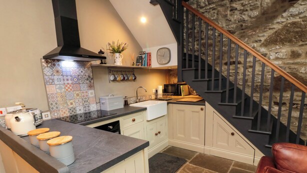 A kitchen with a black stove, white cabinets, and a stone floor. - Ash Cottage (Barnard Castle)