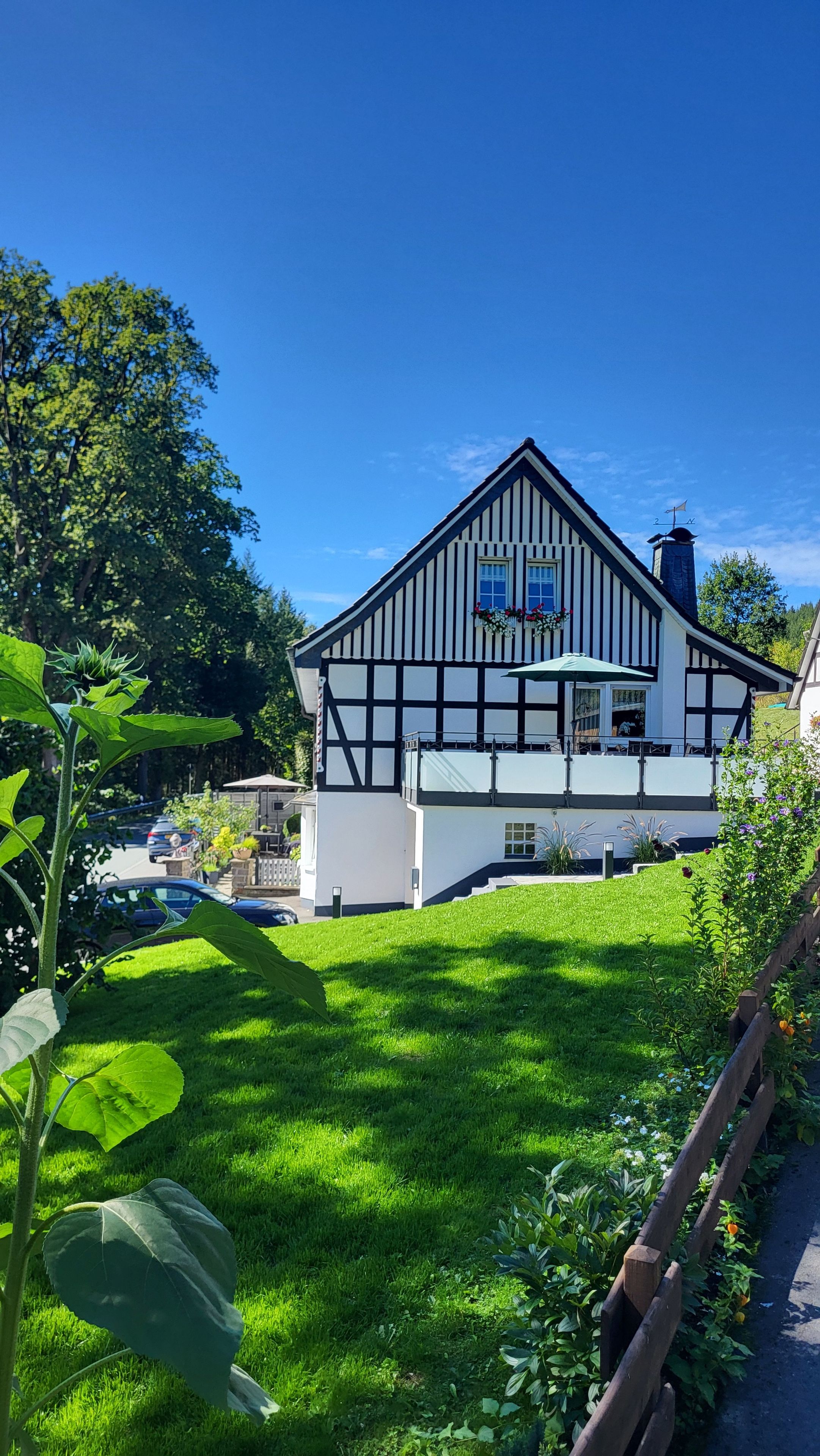 Ein traditionelles Fachwerkhäuschen mit Balkon, umgeben von einem gepflegten Rasen und Garten.