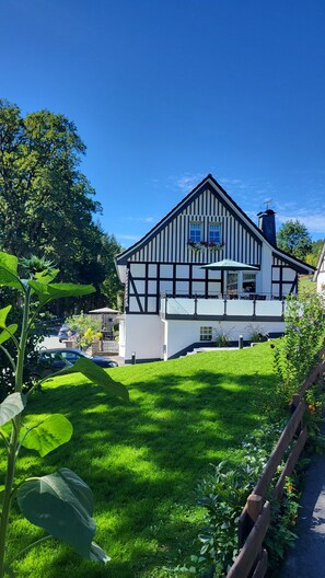 A traditional half-timbered house with a balcony, surrounded by a well-maintained lawn and garden. - Apartment 'Krähling' with Mountain View, Shared Terrace and Wi-Fi (Schmallenberg)