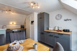 A modern kitchen with grey cabinets, a wooden dining table, and a clock on the wall.