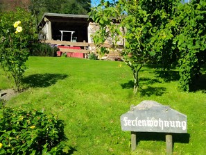 A sign reading 'Seifenmohnung' in a garden with a wooden structure in the background.