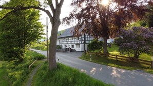 A traditional half-timbered building with a paved driveway and a grassy area with trees. - Apartment 'Krähling' with Mountain View, Shared Terrace and Wi-Fi (Schmallenberg)