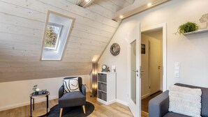 A room with a sloped ceiling, a skylight, a grey sofa, a small round table with a plant, and a bookshelf. - Apartment 'Krähling' with Mountain View, Shared Terrace and Wi-Fi (Schmallenberg)