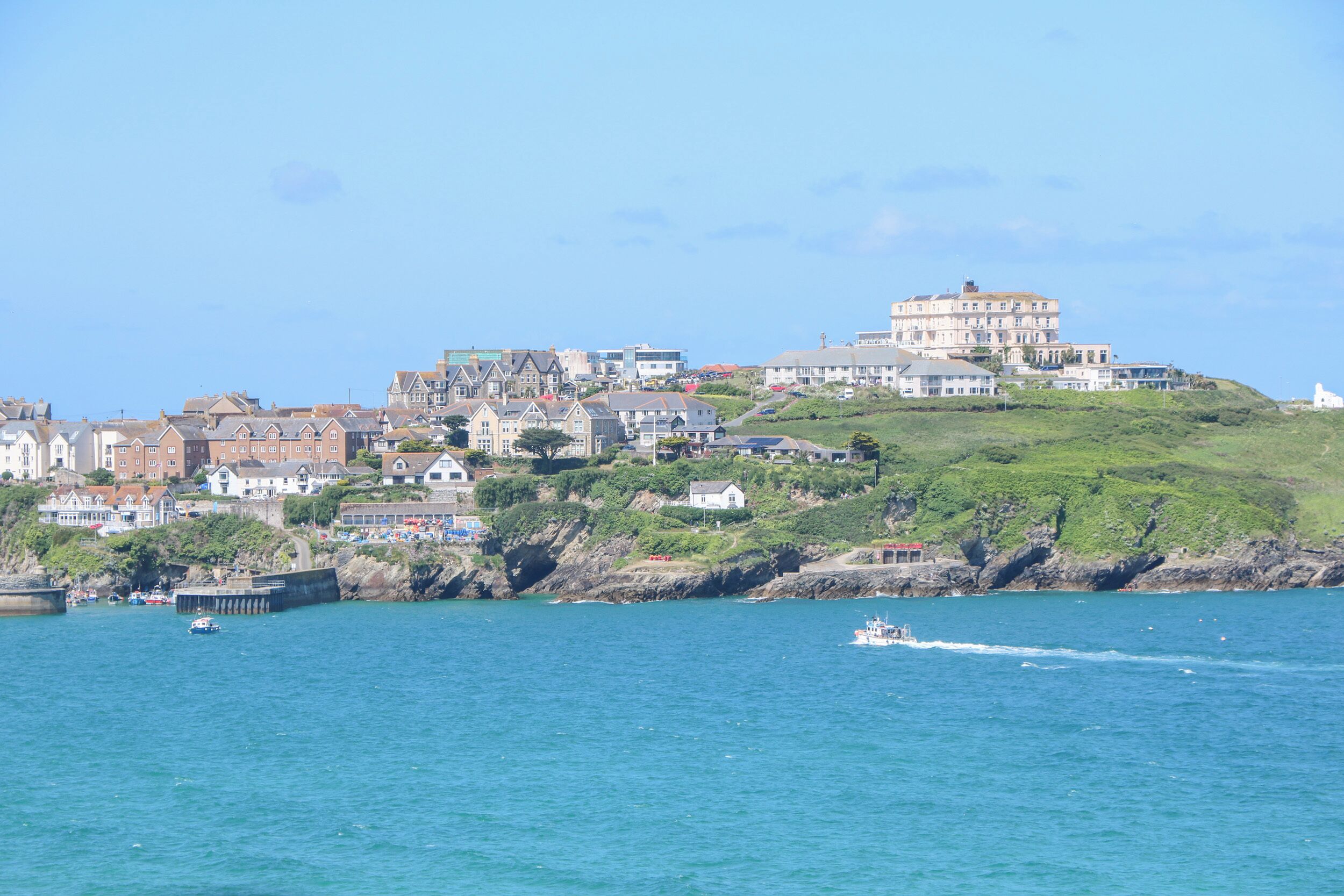 A coastal town with a prominent building on a hill, a pier, and a boat in the water.