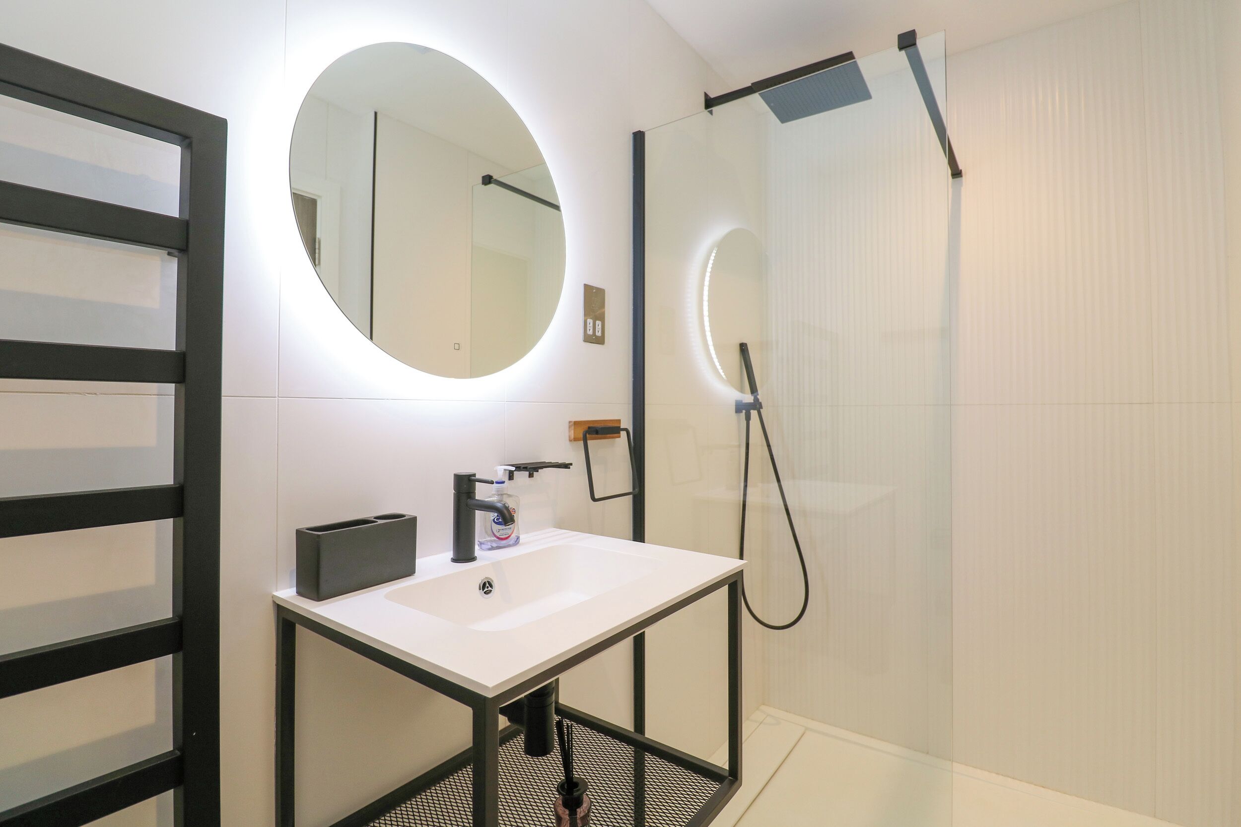 A modern bathroom with a white sink, a round mirror, and a glass shower enclosure.