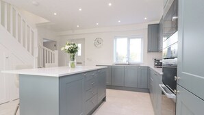 A modern kitchen with grey cabinets, a white countertop, and a vase with flowers. - Apple Tree Cottage (Preston)