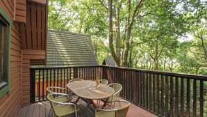 Une terrasse en bois, agrémentée d’une table et de chaises, entourée d’une balustrade en bois, et offrant une vue sur une zone boisée.