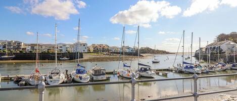 A marina with various boats docked, a clear sky, and buildings in the background.