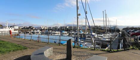 A marina with boats docked along the water, a stone structure in the foreground, and a clear sky.