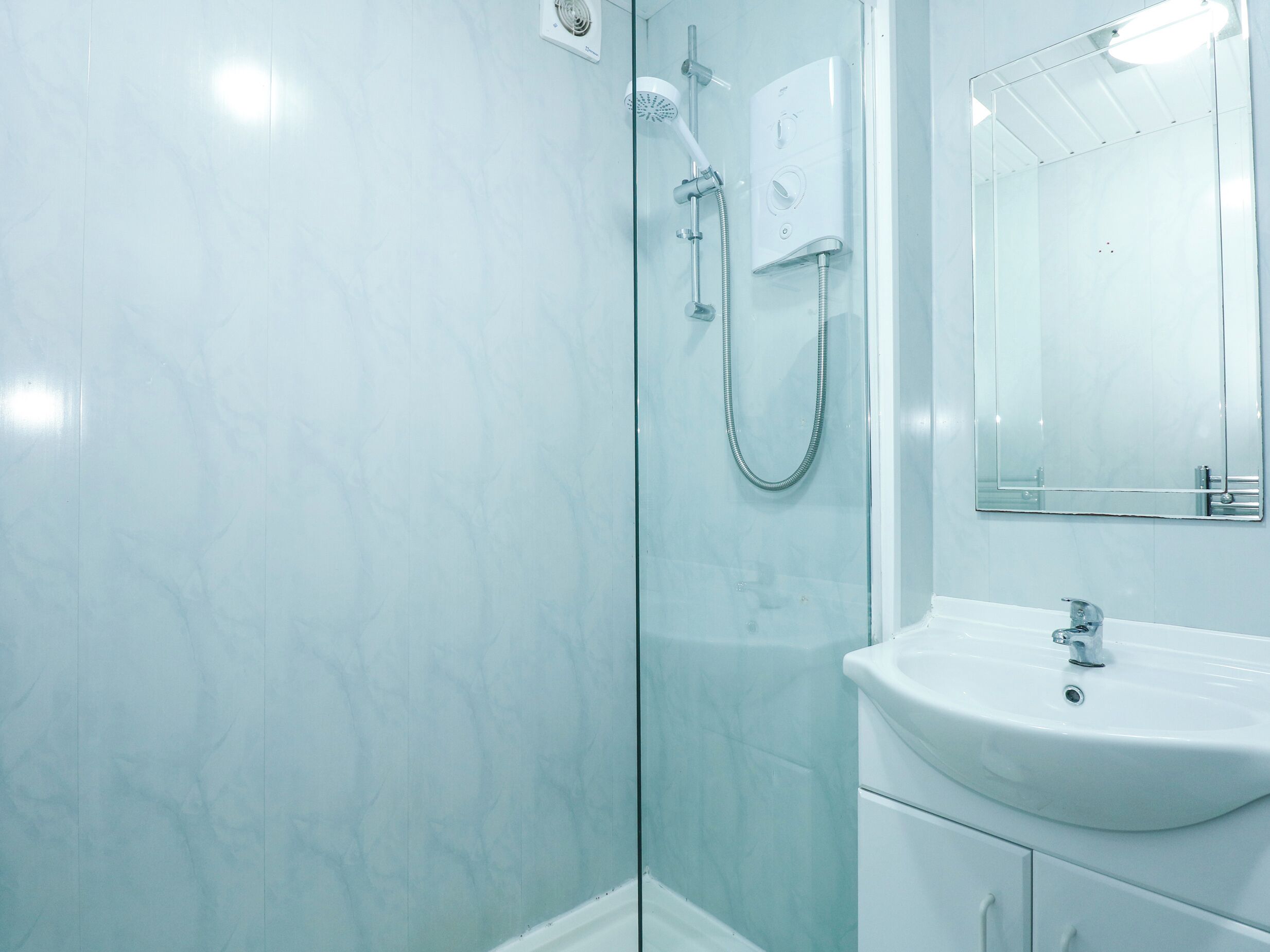 A bathroom with a glass shower enclosure, a white sink, and a mirror.