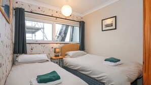 Une chambre avec deux lits, une fenêtre avec des rideaux, une lampe et un tableau encadré au mur.