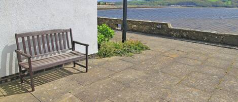 A bench against a white wall with a view of a body of water and distant hills.