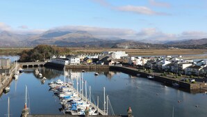 Un port de plaisance avec des bateaux amarrés, une ville avec des bâtiments et des montagnes en arrière-plan.