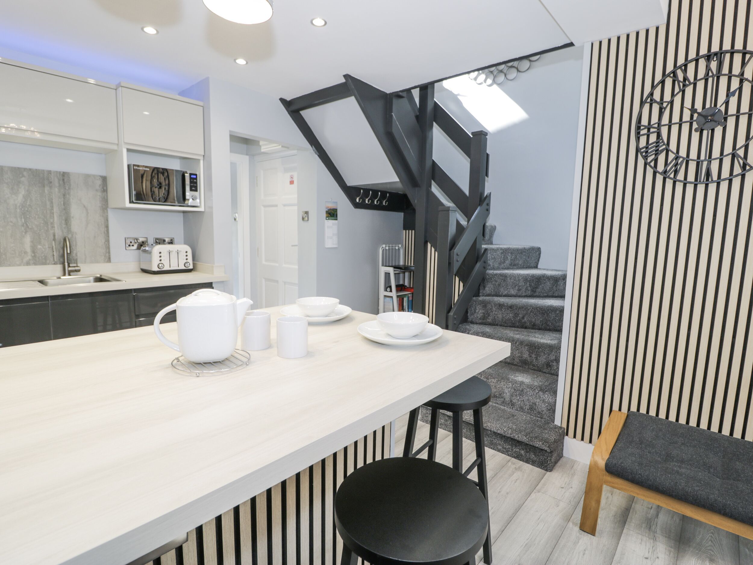 A modern kitchen with a wooden island, a staircase, and a clock on the wall.